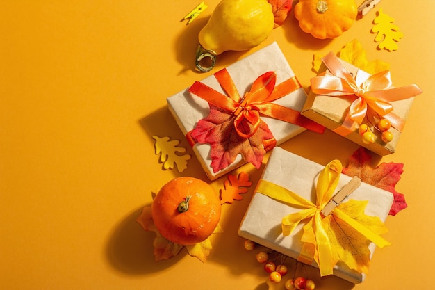 Gift concept in autumn colors. Wrapped boxes, festive fall decor, pumpkin, leaves, and berries. A trendy hard light, dark shadow, orange background, top view