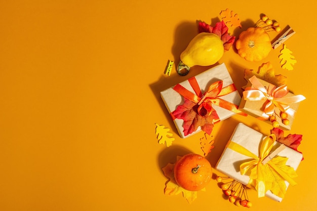 写真 秋の色のギフトコンセプト。包まれた箱、お祝いの秋の装飾、カボチャ、葉、そしてベリー。トレンディなハードライト、暗い影、オレンジ色の背景、上面図