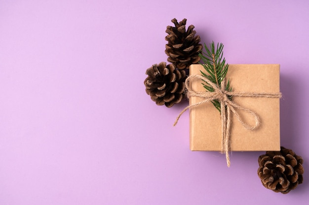 Gift craft box with Christmas decoration from fir branches in cones on a purple background with copy space. Top view