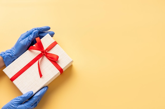 Gift delivery Pandemic hygiene Hands in protective gloves holding present box taped red ribbon Isolated on beige copy space New normal Festive background COVID19 prevention