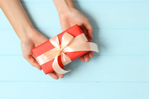 Gift in female hands on a colored background top view