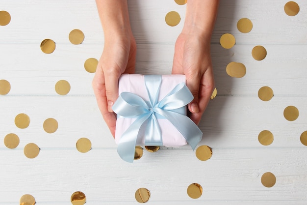 Gift in female hands on a colored background with confetti top view