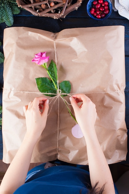 Regalo in carta da regalo grigia e una rosa rosa, in mani femminili