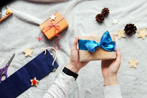 Gift in hand. Gift wrapping process. Blue bow. Gifts in craft paper. Festive atmosphere. New Year's decor. Minimalistic gift wrapping