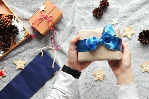 Gift in hand. Gift wrapping process. Blue bow. Gifts in craft paper. Festive atmosphere