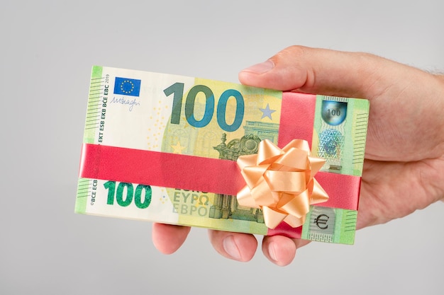 Dono di denaro un pacchetto di banconote da 100 euro in mano a un uomo concetto di regalo di denaro per il compleanno o il natale regala euro con il nastro regalo