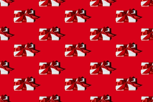 Фото Шаблон подарка. красный бесшовный фон. праздничный декор. дальнее настоящее. симметричная композиция из белых коробок с ленточными бантами, изолированными на ярком.