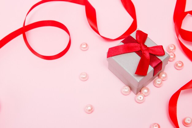 Gift on a pink background with beads and a red ribbon.