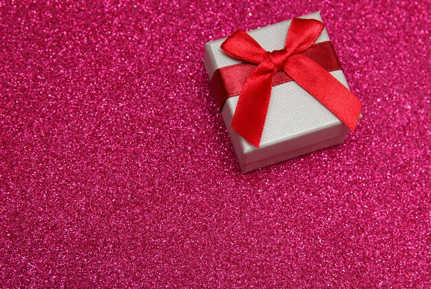 Gift pink box on glittering pink background.