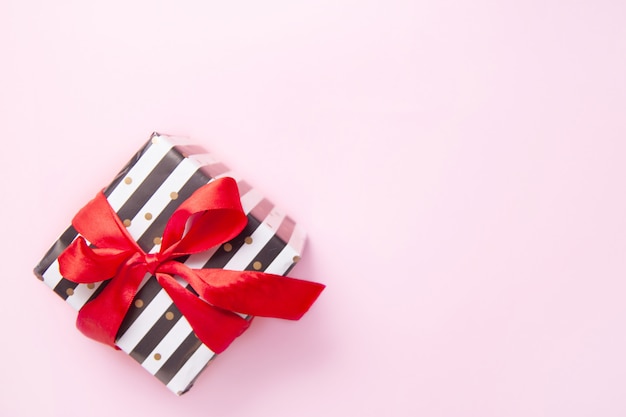 Gift or present box in white and black stripes with a red ribbon bow isolated on pink table top view