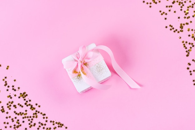 Gift or present box with confetti stars and pink ribbon on pastel pink color. Flat lay style.