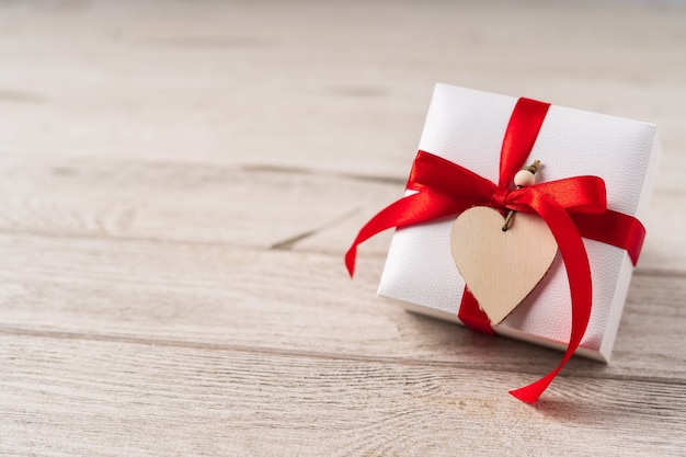 Gift or present box with red bow and heart on wooden background