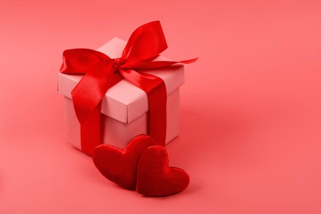 Gift or present box with red bow ribbon and glitter heart on living coral background for Valentines day