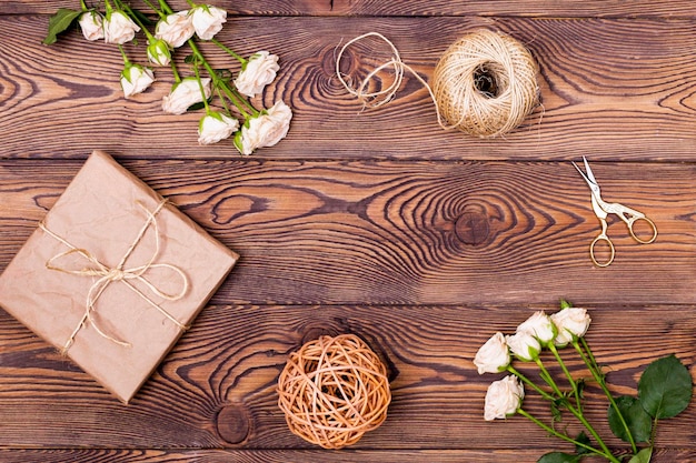 Gift or present box wrapped in kraft paper and flower twine and scissors on wooden background from above Flat lay styling