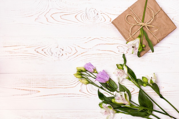 Gift or present box wrapped in kraft paper and flower on white table from above Flat lay copy space