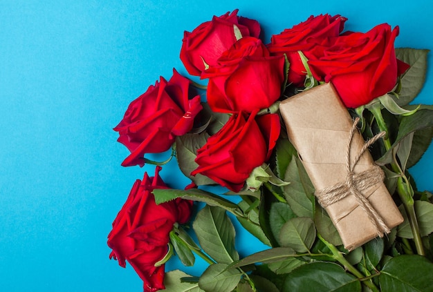 Gift or present box wrapped in kraft paper and roses on blue background. Flat lay styling. Copy space for text.