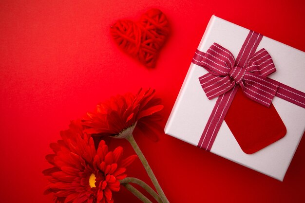 Regalo, gerbere rosse e un cuore su sfondo rosso. concetto di amore per san valentino.