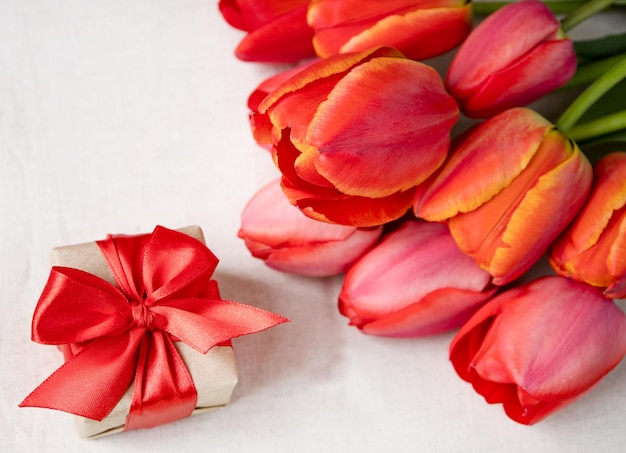 Un regalo e tulipani rossi su sfondo chiaroil concetto di cura e celebrazione dell'amore
