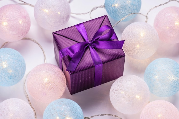 Gift in a shiny purple box and glowing Christmas balls Festive mood christmas concept