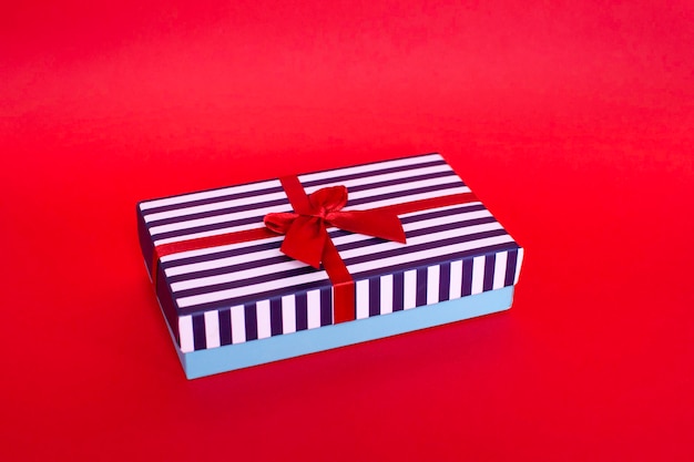 Gift striped box with a red satin bow on the red background.