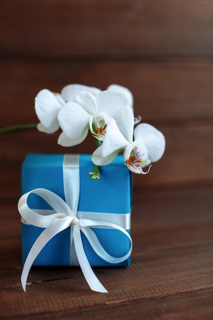 Gift and white orchid on a wooden background. 