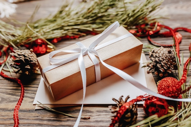 Gift with blank note with fir branch and Christmas toys on wooden background. New Year concept