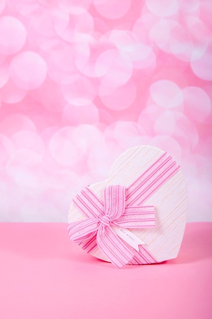 Gift with a bow in the form of a heart on a pink background with bokeh