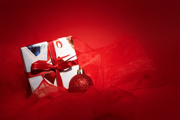 A gift with a red ribbon and a Christmas tree toy on a red New Year's background