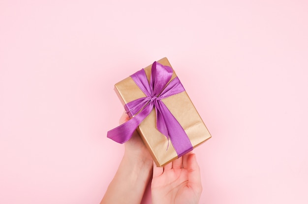 Gift wrap in the hands of a girl, top view. flat lay on pink background, woman gives a present for christmas or birthday