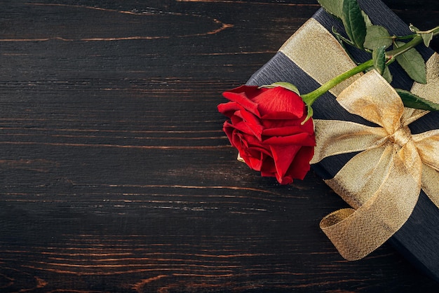 Gift wrapped in black paper and a gold ribbon. on top of the box is a luxurious red rose. The concept of an expensive gift for the holiday Valentine's Day or Women's Day March 8