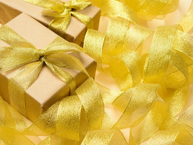Regalo avvolto in carta marrone su uno sfondo di nastro dorato ritorto, sfondo festivo, vista dall'alto