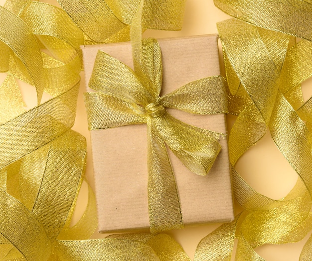 Gift wrapped in brown paper on a twisted golden ribbon, top view