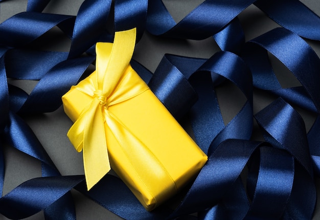 Photo gift wrapped in yellow paper on curled blue ribbon background, festive background, top view