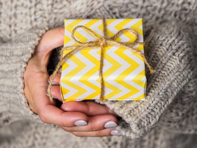 A gift wrapped in yellow paper lies in the hands of woman