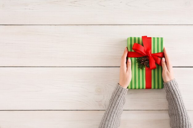 Photo gift wrapping background. female hands holding handmade present box in striped paper against white wooden table background. bithday or christmas preparation concept, top view, copy space