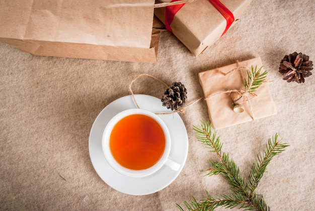 Confezioni regalo e lettere, cartoline per auguri di natale. buste con lettere, regali, rami di alberi di natale e pigne sono su una bugia di tavolo in legno, una tazza di tè caldo profumato, vista dall'alto