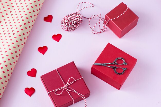 Gift wrapping paper, scissors, ribbon, three red gift boxes and satin hearts