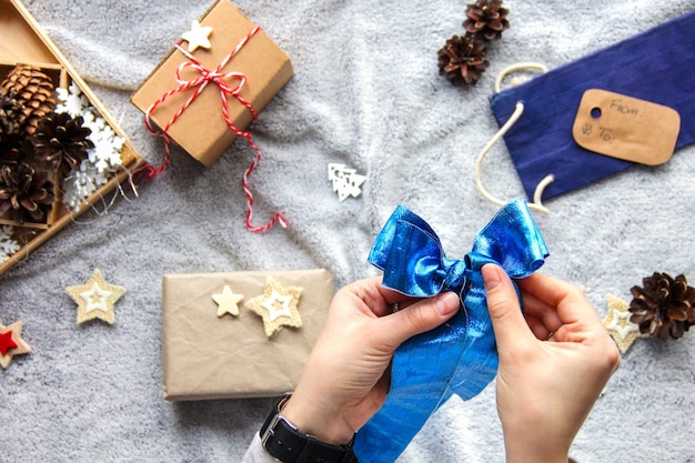 Gift wrapping process. Blue bow. Gifts in craft paper. Festive atmosphere. New Year's decor. Minimalistic gift wrapping