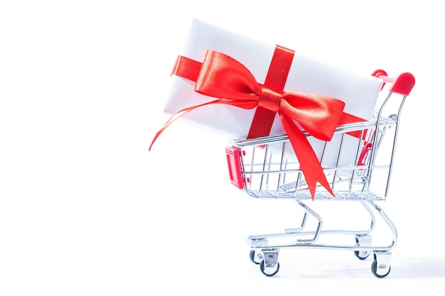 Giftbox with red ribbon and bow in shopping cart isolated on white