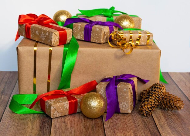 Gifts are packed in kraft paper and tied with a satin ribbon with New Year's toys and cones on a wooden background Toys for the Christmas tree