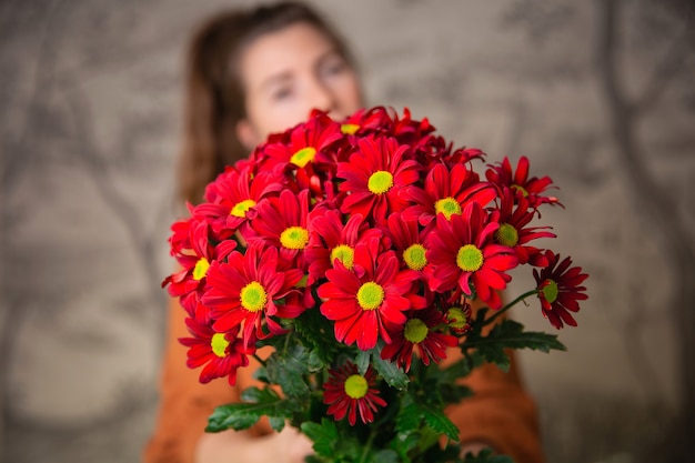 ギフト、お祝い、優しさのコンセプト。赤い花の花束、バレンタインデーのデイジーを持って驚いたかわいい若い女性