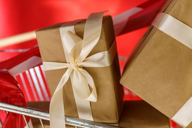 Gifts in craft paper with white tape in a supermarket trolley on a red background