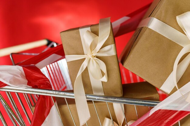 Gifts in craft paper with white tape in a supermarket trolley on a red background