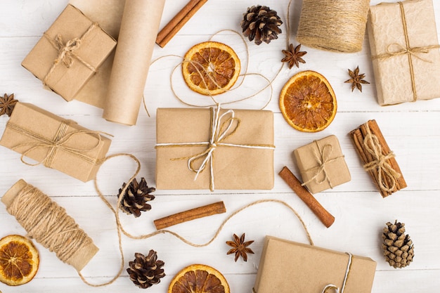 Фото Подарки из крафт-бумаги, сушеных апельсинов, корицы, сосновых шишек, аниса на белом столе