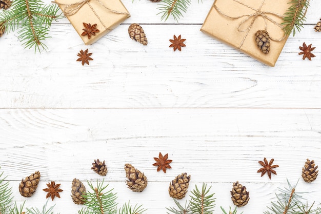 Gifts for new year wrapped in craft paper near spruce branches and cones on white wooden background top view copyspace