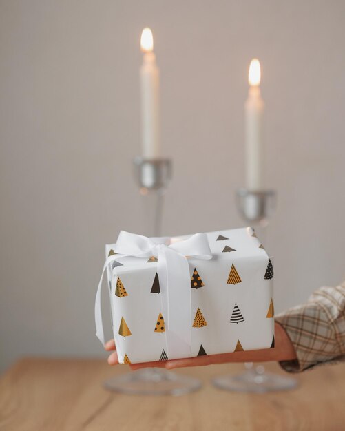 Gifts in white packaging are on the table against the background of candles a womans hand holds