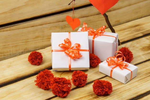 Gifts in white wrapping are tied with a red ribbon on a wooden surface