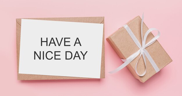 Gifts with note letter on isolated pink surface with text HAVE A NICE DAY