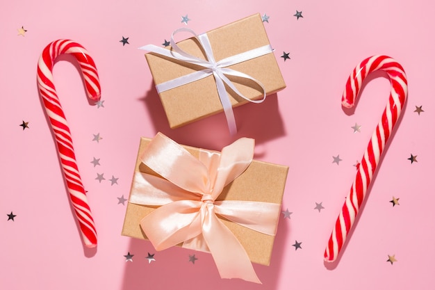 Gifts with red Christmas candies and confetti stars pours on a pastel pink background, top view. Flat lay. Holiday new year, celebration atmosphere concept