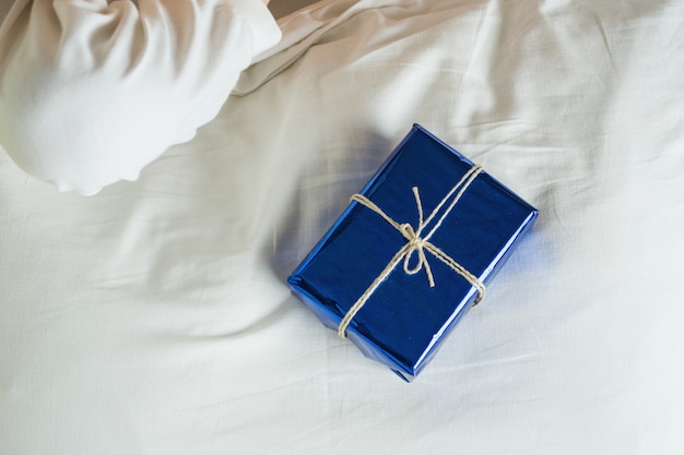 Giftverrassing in bed, blauwe ingepakte doos op wit bed